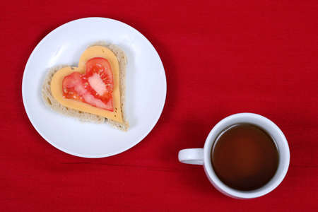 Heart shape sandwich on white plate and a cup of tea, on red backgroundの写真素材