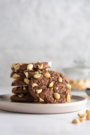 Cracked chocolate chip cookies with pieces of roasted peanuts on a ceramic plate with nuts in a blur on the background. Close-up with space for text.の写真素材