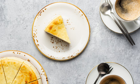 Top view of a piece of cottage cheese casserole with cups of coffee on ceramic plates with cutlery on a light concrete gray background. Coffee break concept with cheesecake.の写真素材