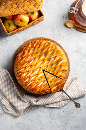 Yeast pie with apples and cottage cheese with a lattice crust, with a basket of apples and a teapot of tea on a concrete gray background. Sliced piece of cake on a spatula. top view.の写真素材