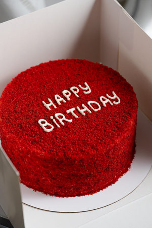 Close-up of a red velvet birthday cake with Happy Birthday written on top, presented in a white box....