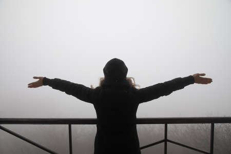 silhouette of a female with widely open hands looking towards fog mist. ladyの写真素材