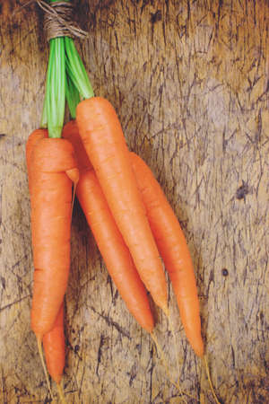 Bunch of fresh carrots with green leaves over wooden backgroundの写真素材