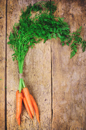 Bunch of fresh carrots with green leaves over wooden backgroundの写真素材