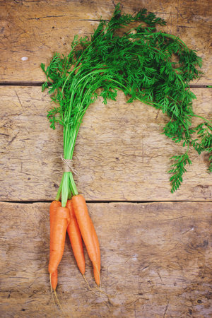 Fresh carrots with green leaves over wooden background