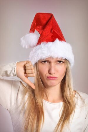 Beautiful Christmas woman with thumbs down sign. Disappointed girl with Santa hatの写真素材