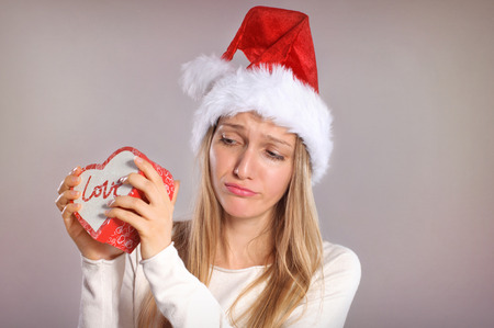 Disappointed Christmas woman with a Santa hat holding a gift boxの写真素材
