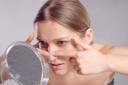 Young woman squeeze her acne in front of the mirror. Woman skin care conceptの写真素材