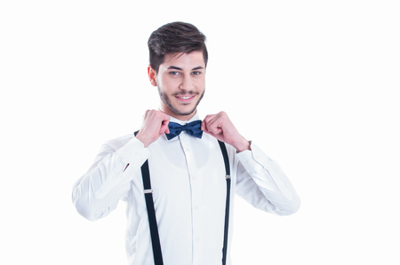 Young man correcting his bow tie, smiling. Isolated on white backgroundの写真素材