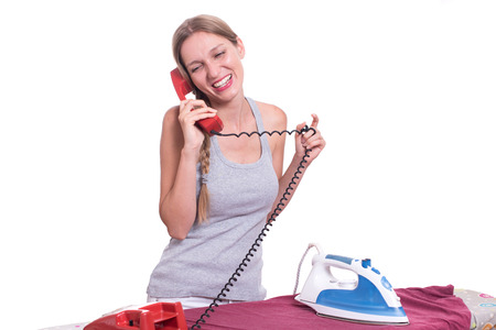 Young woman talking on the phone while ironing clothesの写真素材