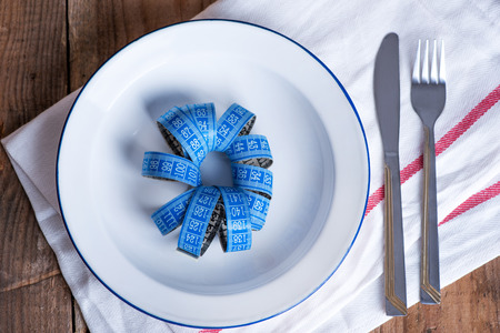 Concept diet and weight loss. Empty plate with measuring tape in the middle of the plateの写真素材