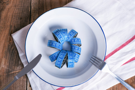 Concept diet and weight loss. Empty plate with measuring tape in the middle of the plateの写真素材