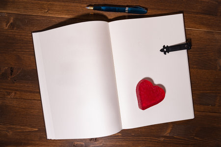 dark table with vintage book and pen next to a heartの写真素材
