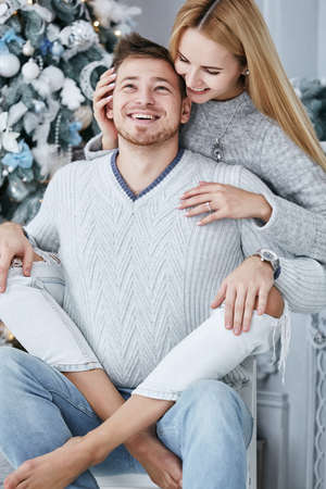 Love story of beautiful couple in studio near Christmas tree. Girl and boy in blue sweaters. Girl and boy in love. Hugging couple. Winter love story in studio.の写真素材