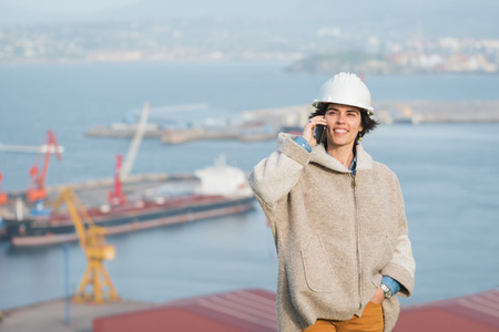 successful independent engineer smiling woman on industrial harbor with safety helmet talking on the phone. Pioneer woman at work.の写真素材
