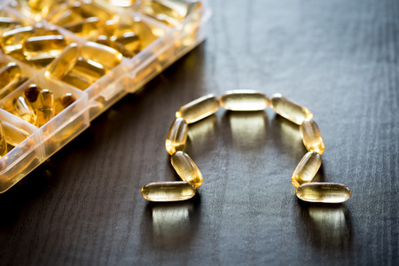 Omega 3-6-9 fish oil yellow softgels drawing omega letter on wooden black table. Daily pill box.の写真素材