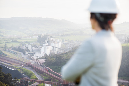 Thoughtful successful independent engineer woman on industrial area with safety helmet showing back. Pioneer woman at work.の写真素材