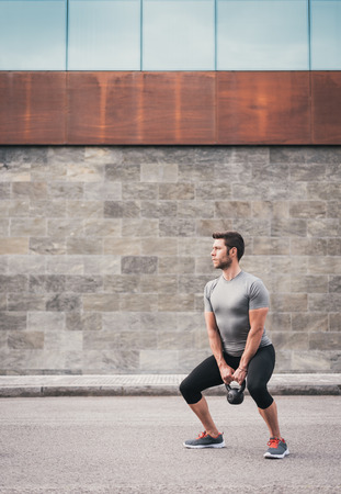 Fitness male working out legs with kettlebell. Sporty man working out outdoor on asphalt.の写真素材