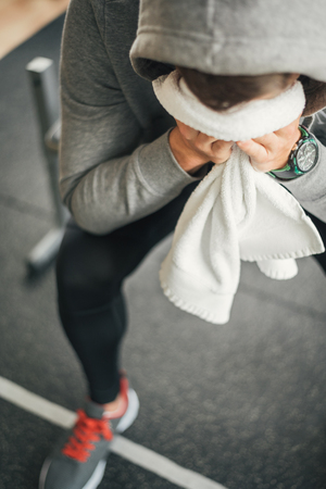 Strong sporty man sitting on gym bench with towel on face, suffering breakdown to overcome. Frustration sport concept.の写真素材