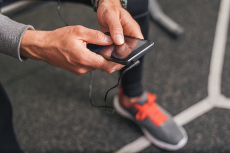 Smartphone closeup at the gym. Sporty man using phone and listening music for motivation before workout.の写真素材