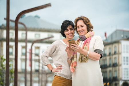 Two women looking at screen of phone at urban landscape. Urban female lifestyle.