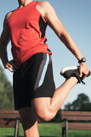 Fitness man close up stretching legs before outdoor workout. Sporty male athlete in an urban park...