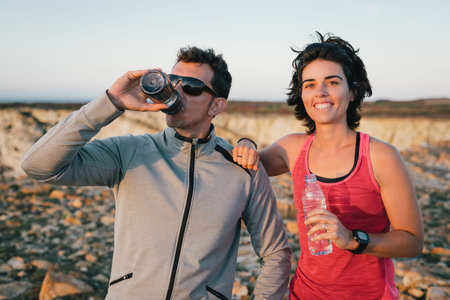 Fitness sport running couple resting and drinking water outside smiling after exercise workout