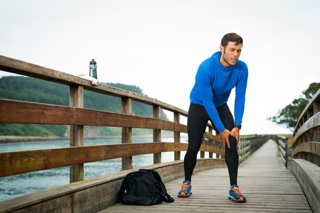 Fit runner sportsman holding knee in pain in a park. Broken twisted joint running sport injury. Athletic man touching leg due to sprain. Rodiles, Asturias.の写真素材