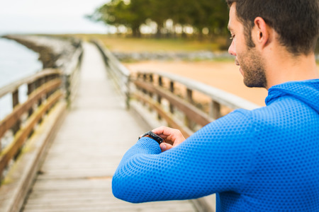 Strong smiling sportsman adjusting sport watch for an outdoor running training on a cloudy autumn day on a wooden walkway. Fitness sporty man in Rodiles, Asturias.の写真素材