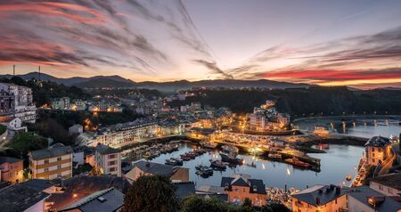 Touristic destination Luarca, Asturias, Spain, Europe. Nature urban landscape with fishing and pleasure port with boats, harbor, sea and beach. Gorgeous red sky at sunset with beautiful sky clouds.の写真素材