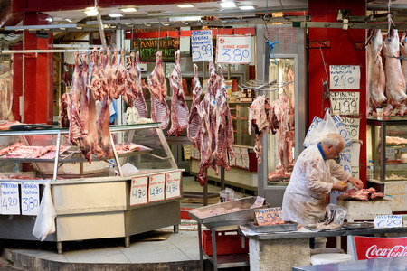 Thessaloniki, Greece - April 14, 2017 : Butcher preparing raw meat for sale on meat market and several hanging lambs in backgroundのeditorial素材