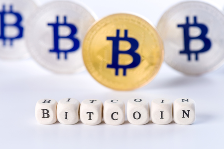 Single word BITCOIN made of wooden blocks with several golden and silver colored Bitcoin coins standing on white background, cryptocurrency conceptの写真素材