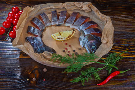A dish of chopped slices smoked fareli with tomato, lemon, dill and red pepper on a wooden background.の写真素材