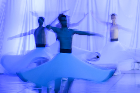 Whirling Dervishes in white and in a religious trance performing on a Turkish stage.の写真素材
