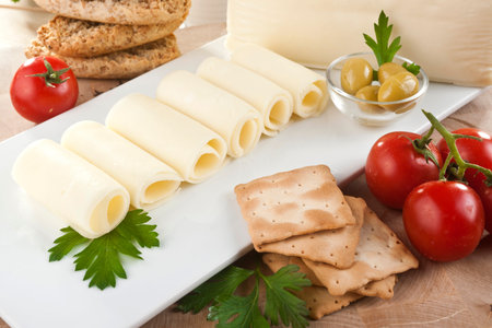 A block of cheddar cheese and cheese slices with a cheese slicer.