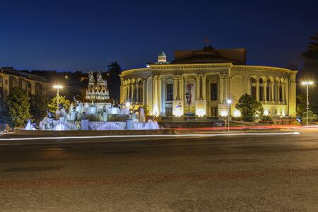 Kutaisi, Georgia - May 5, 2013: Detail from the central square in Kutiasi. People are looking at water fountain, taking pictures or sitting on its edge. In centre is fountain while in background are some buildings and trees from park. Above everything is のeditorial素材