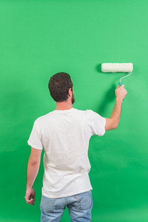 Back view of young man painting the wall with paint roller on green backgroundの写真素材