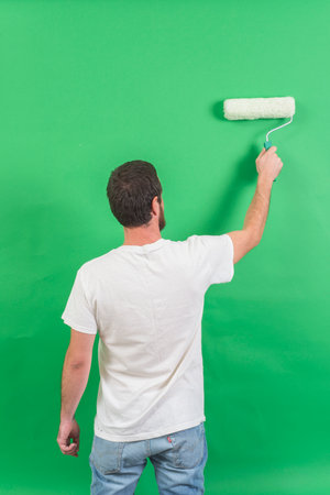 Man painting wall with paint roller. Isolated on green background.の写真素材