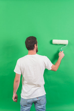 Young man painting the wall with paint roller on a green background.の写真素材
