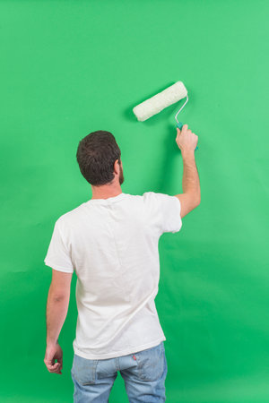 Man paints the wall with a paint roller. On a green backgroundの写真素材