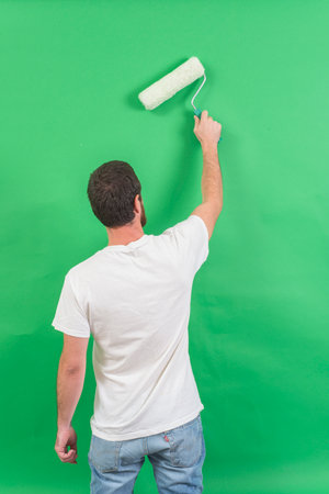 Man painting wall with paint roller. Isolated on green background.の写真素材