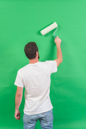 man paints the wall with a roller in his hands on a green backgroundの写真素材
