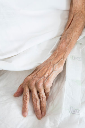 Hands of an elderly woman lying on a bed in the hospitalの写真素材