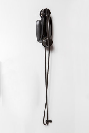 Old black telephone receiver hanging on a white wall, with copy spaceの写真素材
