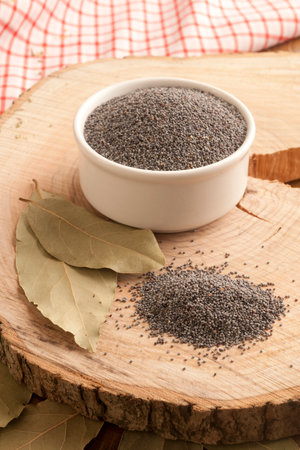 poppy seeds in a bowl and bay leaf on a wooden boardの写真素材