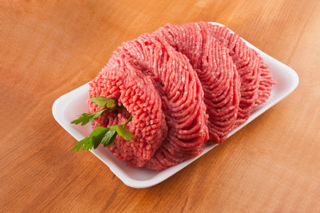 Raw minced beef meat with parsley on a white plate on a wooden background