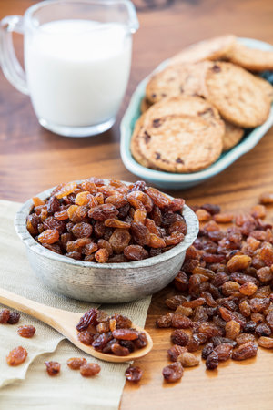 Raisins in a bowl and cookies on a wooden table.の写真素材
