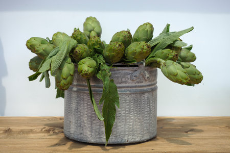 artichokes in a metal bucket on a wooden table with white backgroundの写真素材