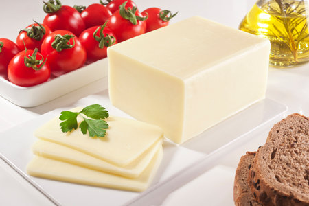 Slices of cheese on a white plate with tomatoes and olive oilの写真素材