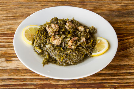 Spinach stew with pork and lemon in white plate on wooden tableの写真素材